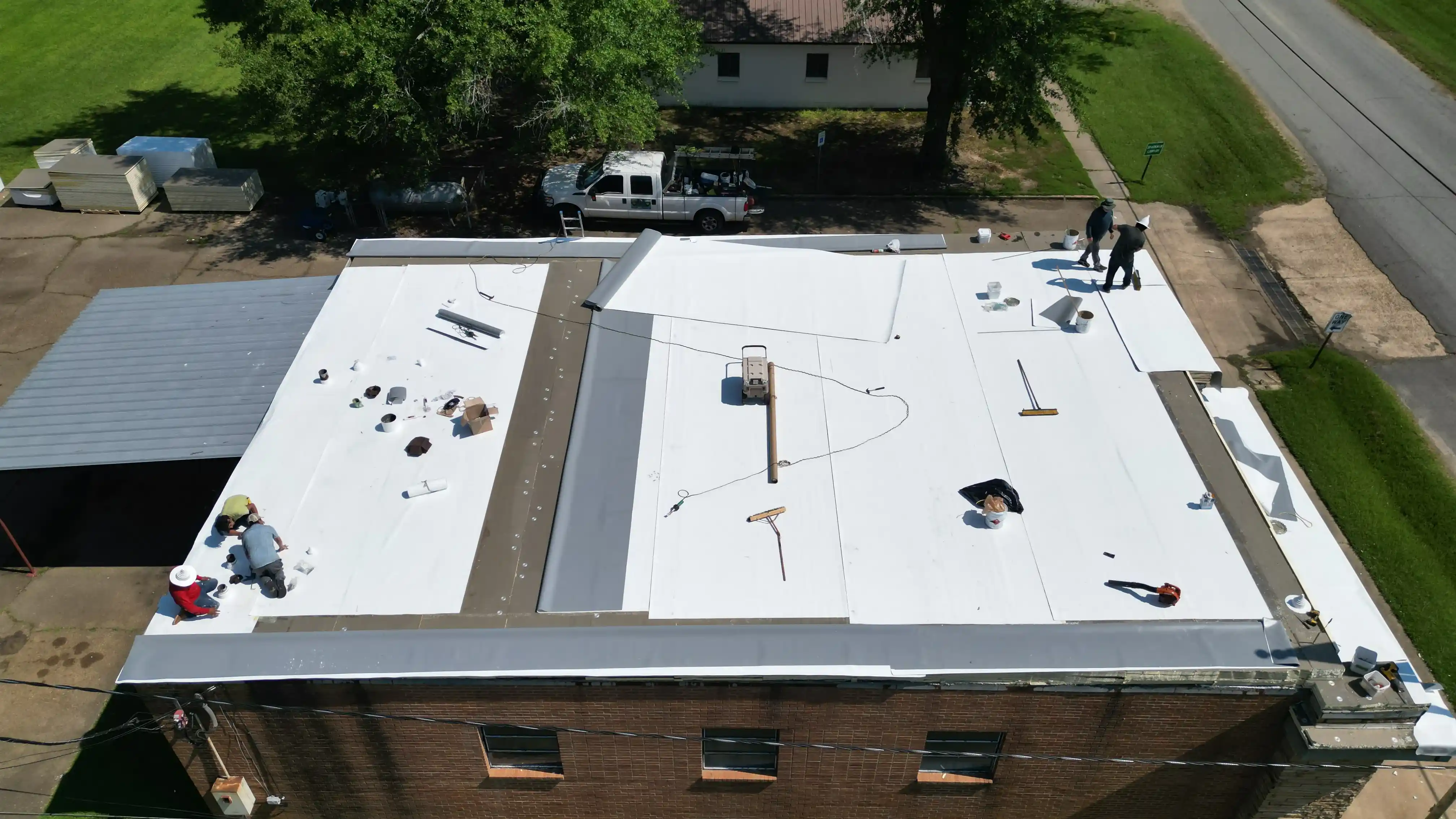 Aerial view of an Ark Roofing crew welding new white membrane across the flat roof of a brick commercial building